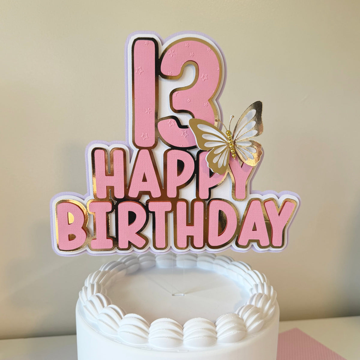 13th birthday cake topper with pink and gold design on a white cake.