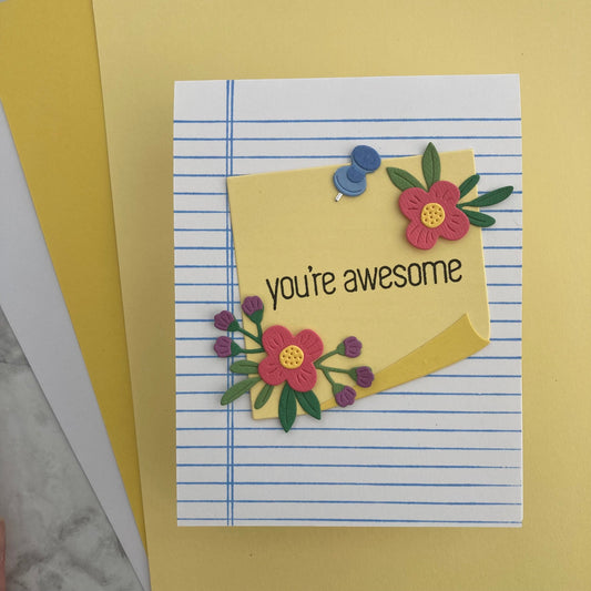 Handmade card with 'you're awesome' text and floral decorations on lined paper.