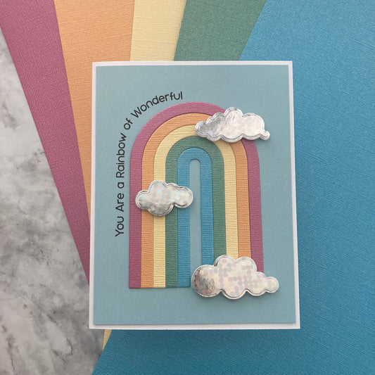 Card with a rainbow design and cloud shapes on a textured surface