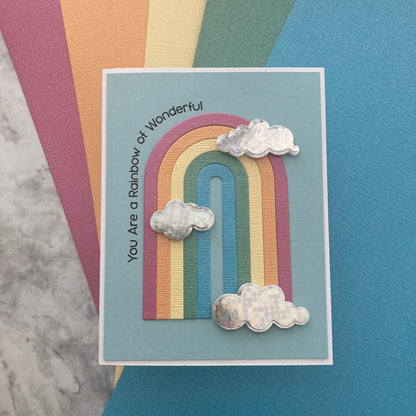 Card with a rainbow design and cloud shapes on a textured surface